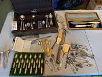 Collector spoons and other silverware arranged on table, showcasing wooden flatware storage box and various spoons along with large serving utensils.