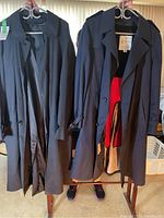 Two navy blue trench coats hanging on hangers; left coat London Fog size 44T, right coat similar style