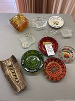 Photo showing all 13 vintage ashtrays including glass, ceramic and souvenir pieces on a table.