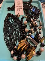 Photo of multiple vintage necklaces and matching earrings on a tray, showing multistrand black bead necklace, black and white bead necklace with earrings, and a black bead necklace with amber geometric pendant and faux pearls.