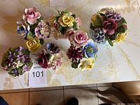 Top view of all six vintage ceramic floral arrangements grouped together on table, showcasing various colorful flower details.