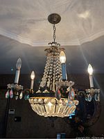 Full view of the vintage chandelier hanging, showing four candle-style bulbs, crystal prisms, and metal frame with some wear and dirt.