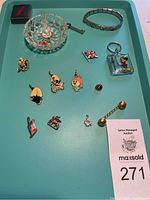 Photo of lot items arranged on a teal tray: silver charms, pins, bracelet, keychain, crystal ring holder, and small ring