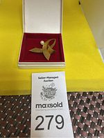 Brooch displayed in open presentation box on red velvet, showing overall form and pearl accent