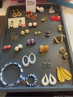 Tray with 24 pairs of assorted vintage pierced earrings in multiple colors and designs plus one matching bracelet and earrings set in blue and white enamel.