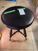 Top view of the black round cushioned piano stool seat showing minor wear and a label with measurements 14" diameter x 18" height.