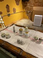 Full view of all 10 antique salt and pepper shakers and 2 small vases arranged on towel in rustic setting