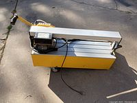 Side and top angle view of yellow and silver QEP 24 inch bridge saw with power cord and handle, placed on a concrete surface.