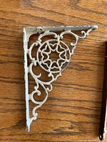 Close-up image of one ornate antique cast iron shelf bracket showing scroll and star design in distressed white paint.
