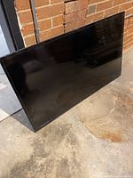 Front view of the 42-inch flat screen TV leaning against a brick wall, reflecting its surroundings on the glossy black screen surface.