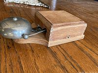 Side angle view showing oak wood casing with tongue and groove edges and metal bell with pull lever attached.