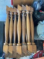View from above showing 9 twisted carved wooden stair spindles with squared and grooved ends, arranged side by side.