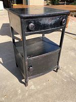 Front-side angle showing the single drawer and lower cabinet with rounded knobs. The cabinet is painted black with visible wear and torn paint.