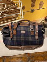 Full view of the British wool and leather duffle bag showing tartan plaid pattern with leather straps and handles