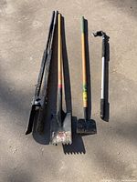 Photo of four garden hand tools arranged vertically on concrete floor: hole shovel, shingle shovel, garden hoe, and gutter cleaner