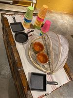 Overview of cast iron pans, plastic party cups, terracotta salsa bowls, and covered serving tray on a cloth-covered table.