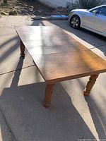 Oak dining room table extended with three leaves on a concrete surface, showing full length and carved legs.
