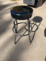 Full view of the black metal shop stool with round seat casting a shadow on the ground