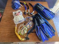 Set of snorkeling gear including masks, snorkels, fins, and bag laid out on a wooden surface.