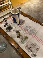 Photo showing overall lot on a table including stoneware vase, whiskey glasses, shot glasses, brass clock, and magnifying glass stand.