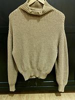 Full view of a beige knitted cowl neck sweater hung on hanger, showing knit texture and style