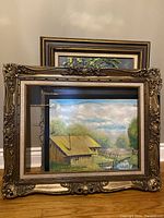 Front view of three original framed landscape paintings stacked, with one in ornate gold frame