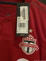 Close-up photo showing tag on red Toronto FC Adidas soccer jersey size S with price tag and team logo.