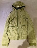 Front view of first army green Aritzia TNA jacket with hood, button and zipper closures, four front flap pockets, ribbed cuffs, and visible TNA logo on the chest.