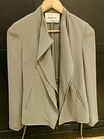 Front view of a light beige/taupe women's jacket with draped collar and front pockets on a hanger.