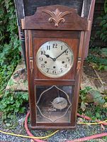Front view of vintage 1940s wooden Westminster chime wall clock showing clock face, carved wood top, and pendulum behind glass door.
