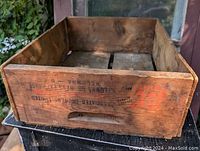 Front angled view of pine fruit box showing interior bottom and handle cut-out with stamped black and red lettering.