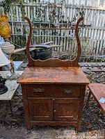 Full view front photo of antique maple washstand showcasing the original finish, curved back frame, drawer with ornate brass handles, and cabinet doors below.