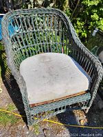 Photo of antique outdoor wicker chair with curved woven wicker frame and stained cushioned seat in outdoor setting.