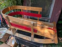 Front side view of a child's antique wooden sleigh showing red painted inside sides and curved wooden backrest.
