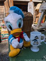 Donald Duck plush stuffed toy and vintage pedestal mug on outdoor table