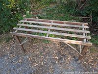 Photo showing the vintage wooden washtub stand with slatted top and angled legs outdoors on gravel and leaves.