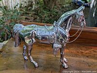Left side view of early nickel plated metal horse figurine showing detailed saddle and chain.