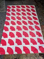 Full view of a large red and white quilt laid out flat on the ground, showing the repeated quarter-circle red shapes on a white background.