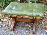 Side angle of the green leather ottoman with wooden base and decorative metal studs.