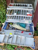 Open view of the blue plastic tackle box showing multiple removable trays with organized compartments containing fishing tackle and accessories.