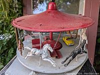 Close-up image of the red metal carousel top with visible horses including white and black ones suspended beneath.