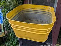 View of old galvanized wash tub showing yellow painted exterior with chipping and wear