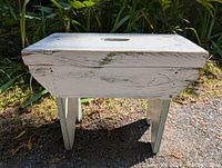 Front view of white painted pine footstool showing rectangular top with carry handle and four angled legs.