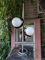 Front and side views of the 1970s retro triple globe chrome table lamp with milk glass globe shades, showing curved chrome features and black Lexan highlights.