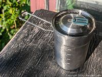 Aluminum camping cooker pot with foldable handle and Stanley-branded lid, showing front and side views with volume markings.