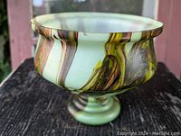 View of vintage glass flower bowl showing swirled green, brown, and yellow colors and flared rim with small chip.