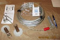 Overview photo of the steel cable coiled with accessories including pulley wheels, mounting hooks, and leather straps. Instruction sheet visible below.