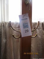 Close-up of two polished brass coat hooks attached side by side to a vertical wooden post, with a MaxSold tag labeled '29'.