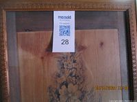 Close-up of framed picture with woodgrain background and floral urn art, showing dust and frame detail.