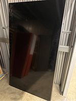 Front view of the TV leaning against metal storage wall, screen off and reflective